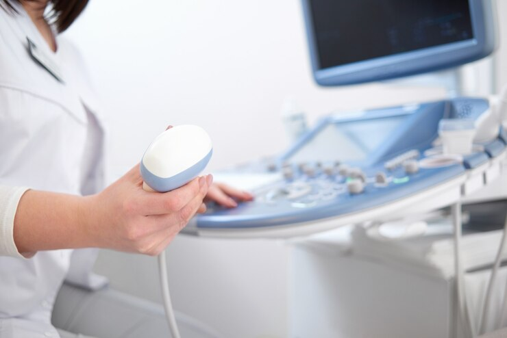 A healthcare professional holds an ultrasound probe near an ultrasound machine.